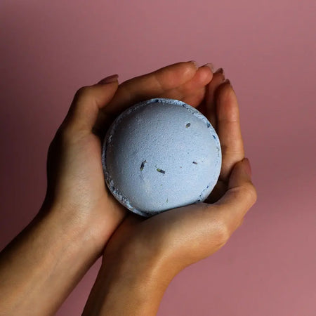 A soft blue round bath bomb with dried herbs embedded in the set of 3 bath bombs lavender and seeds