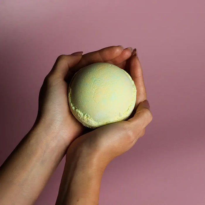 A pale green round bath bomb from a set of 3 bath bombs melon held gently in cupped hands