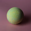 A round bath bomb with a soft mint green base and yellow speckles from the set of 3 bath bombs melon