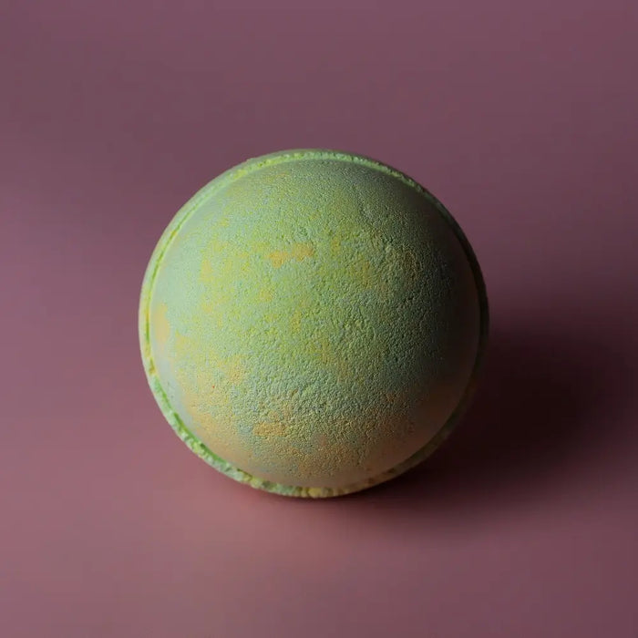 A round bath bomb with a soft mint green base and yellow speckles from the set of 3 bath bombs melon