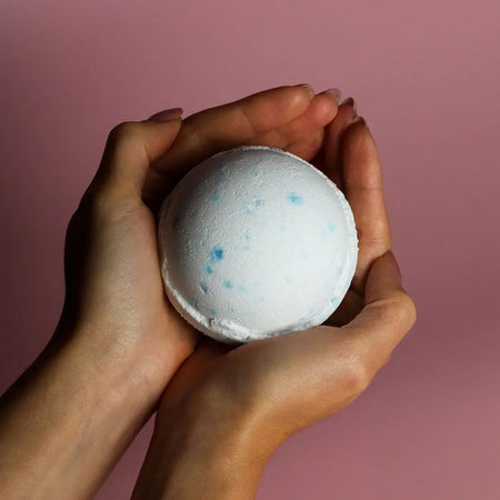 A white bath bomb with blue speckles held in hands from the set of 3 bath bombs ocean collection