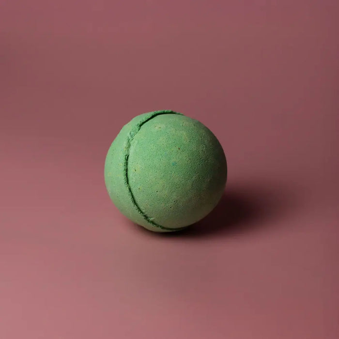 A matte green spherical bath bomb with a subtle texture and seam from a set of 3 peppermint and tea tree bath bombs