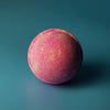 A vibrant pink and yellow speckled bath bomb with a slightly rough texture from a pink lemonade bath bombs set of 3