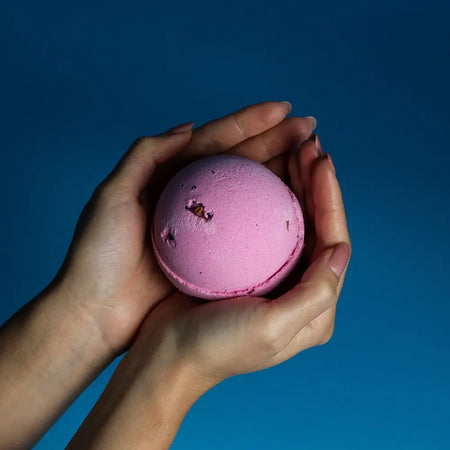 A soft pink spherical bath bomb with rose petals and a textured surface from a set of 3 bath bombs