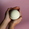 A creamy white speckled simply vanilla bath bomb held gently in cupped hands from a set of 3 bath bombs