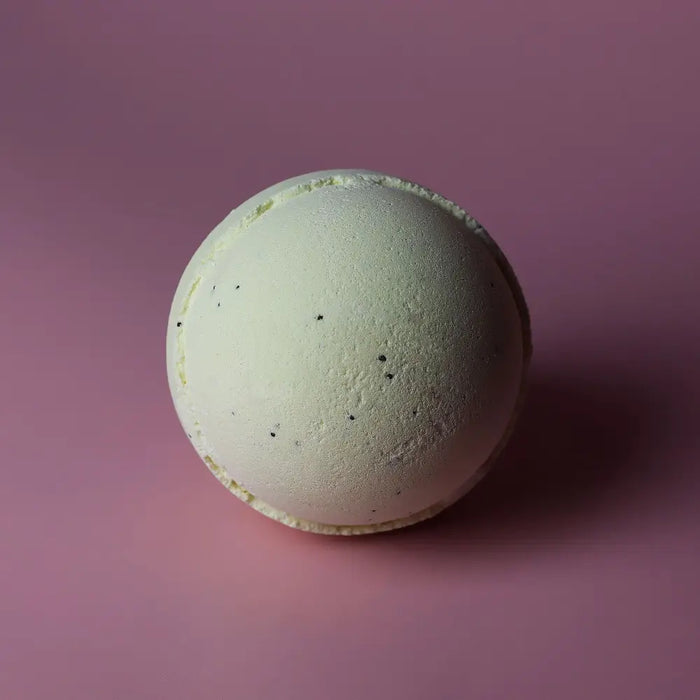 A pale green simply vanilla bath bomb with a rough surface and small dark specks in a set of 3 bath bombs