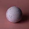 A lavender-colored bath bomb with speckled texture and subtle purple tones from a sweet fennel bath bombs set