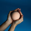 A soft peach-colored spherical bath bomb held in two hands from a set of 3 bath bombs tangerine and grapefruit