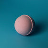 A soft pink spherical bath bomb with a powdery textured surface from a set of 3 bath bombs very berry