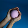 A soft pink round bath bomb held in two hands from a set of 3 bath bombs called very berry