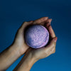 A spherical speckled bath bomb with purple and pink gradient colors from the set of 3 yorkshire violet bath bombs