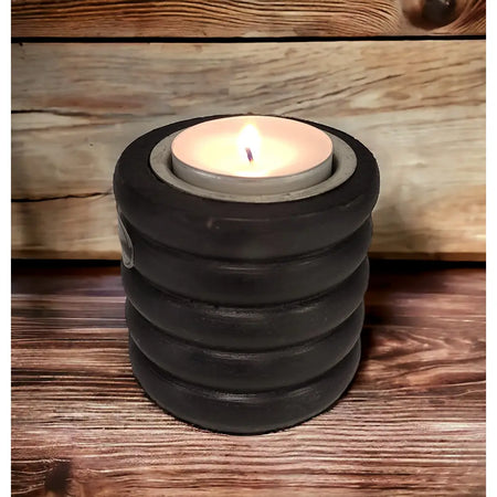 Black stacked ringed concrete tealight holder with a lit candle inside shown on a wooden surface