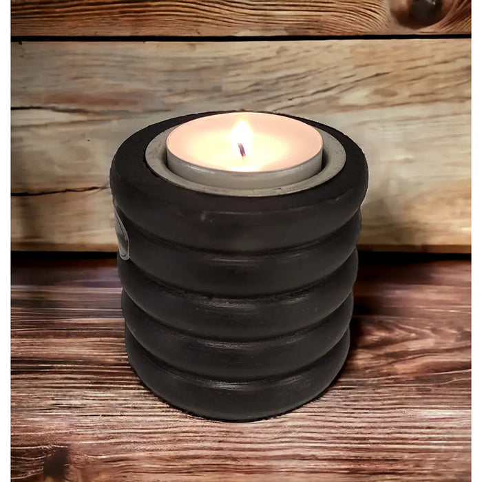 Black stacked ringed concrete tealight holder with a lit candle inside shown on a wooden surface
