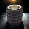 Black suede textured cylindrical air suspension compressor with metallic silver rim shown next to a short ribbed wooden tealight holder