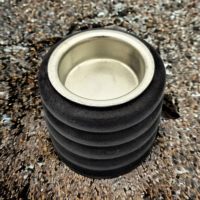 Black rubber door stop with metallic silver rim next to a short ribbed wooden tealight holder on a light surface