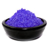 A black ceramic bowl holds vibrant purple blackberry simmering granules with a crystalline texture