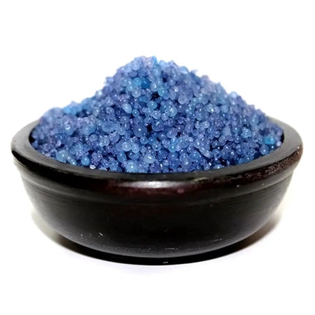A dark wooden bowl filled with vibrant blue crystalline simmering granules for fig and cassis bath use