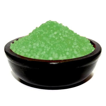 A glossy black ceramic bowl holds a mound of vibrant green translucent pine simmering granules bath salts