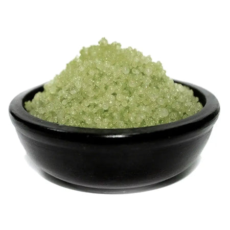 A mound of translucent green simmering granules in a matte black ceramic bowl for sandalwood scent baths