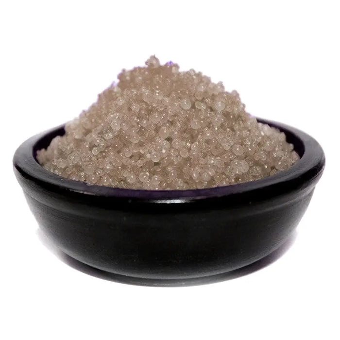A black ceramic bowl holds a mound of translucent light brown simmering granules sandalwood crystals