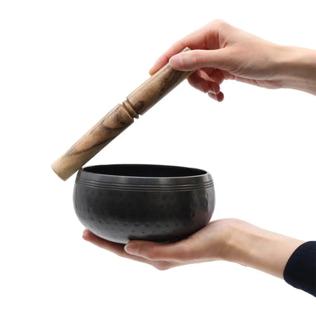 Small black beaten brass singing bowl with dark hammered metal texture and wooden mallet resting on its rim