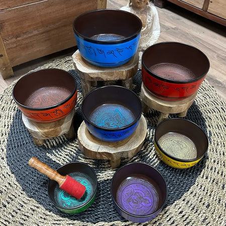 Set of seven colorful tibetan small chakra singing bowls with engraved sanskrit on wooden stands including a blue bowl