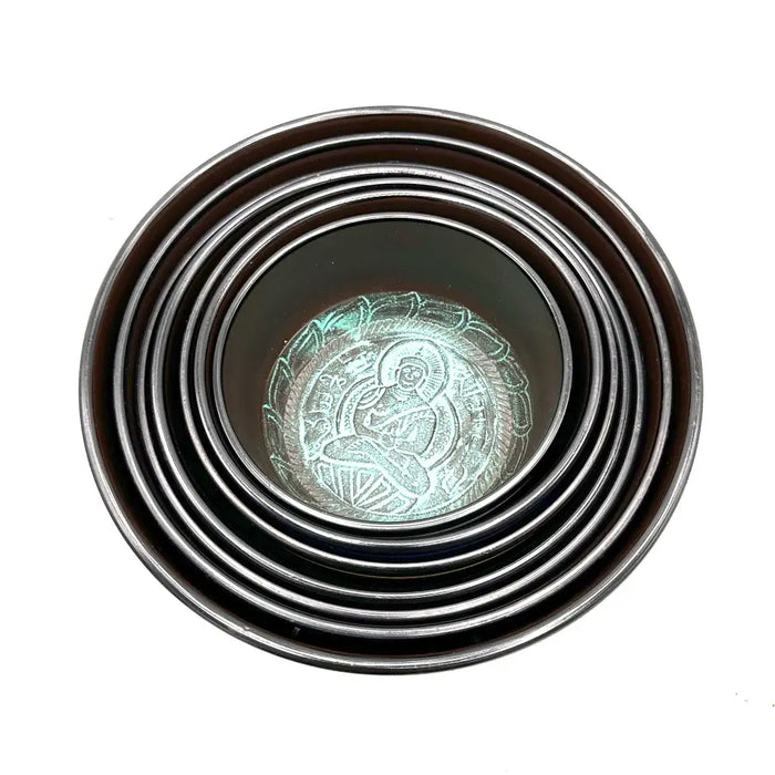 Set of seven singing bowls in dark bronze with a small chakra design and a blue bowl featuring lotus engraving