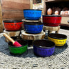 A small chakra set of seven singing bowls in red blue green yellow and purple with black rims and sanskrit script