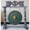 A small green wash bronze gong with a golden center hanging on a dark gray wooden stand with carved dragon heads