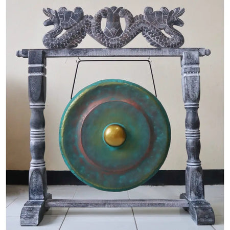 A small green wash bronze gong with a golden center hanging on a dark gray wooden stand with carved dragon heads