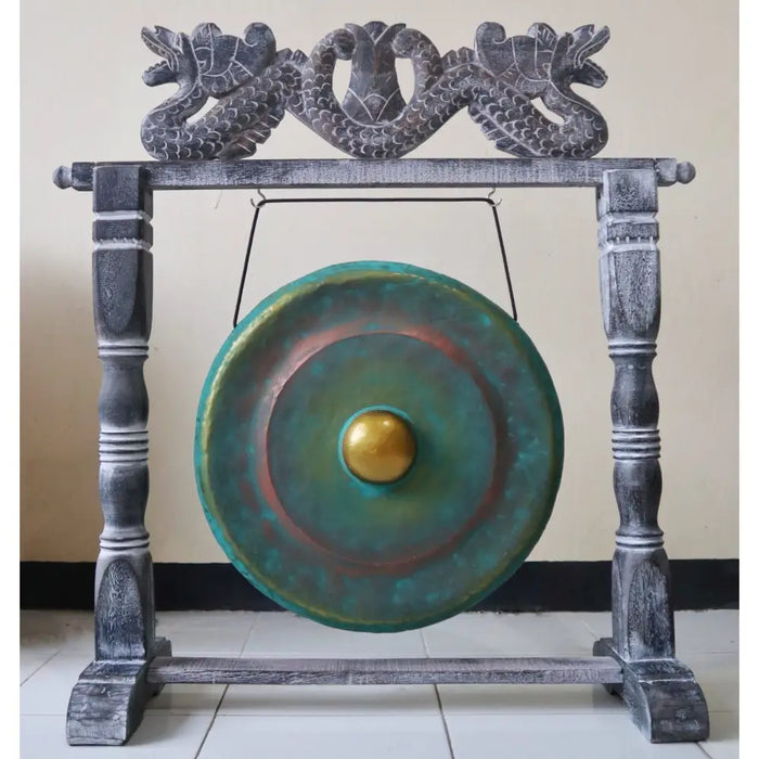 A small green wash bronze gong with a golden center hanging on a dark gray wooden stand with carved dragon heads
