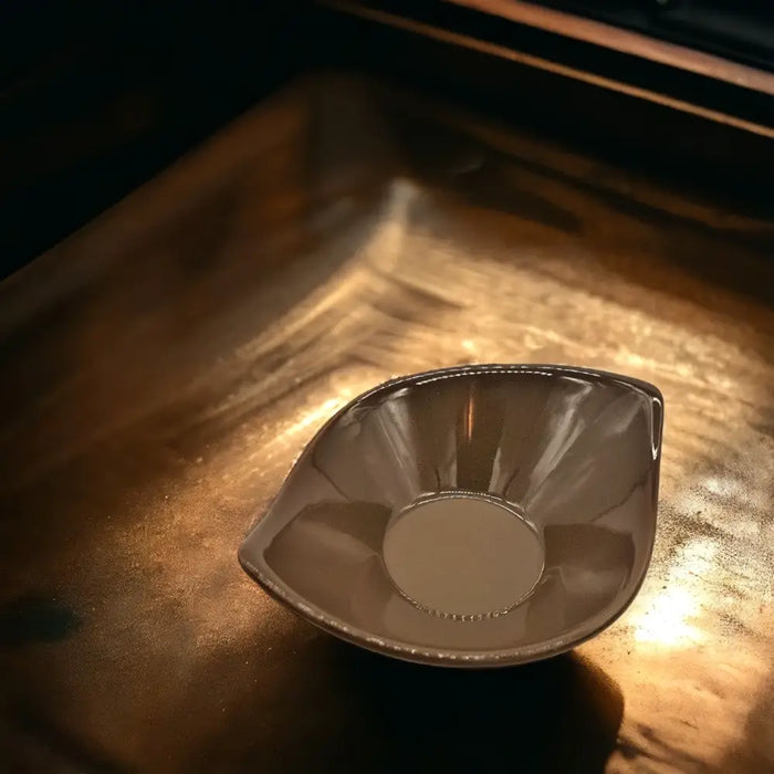 A small leaf-shaped ceramic plate in olive green brown and ivory with a sleek metallic silver bowl on top