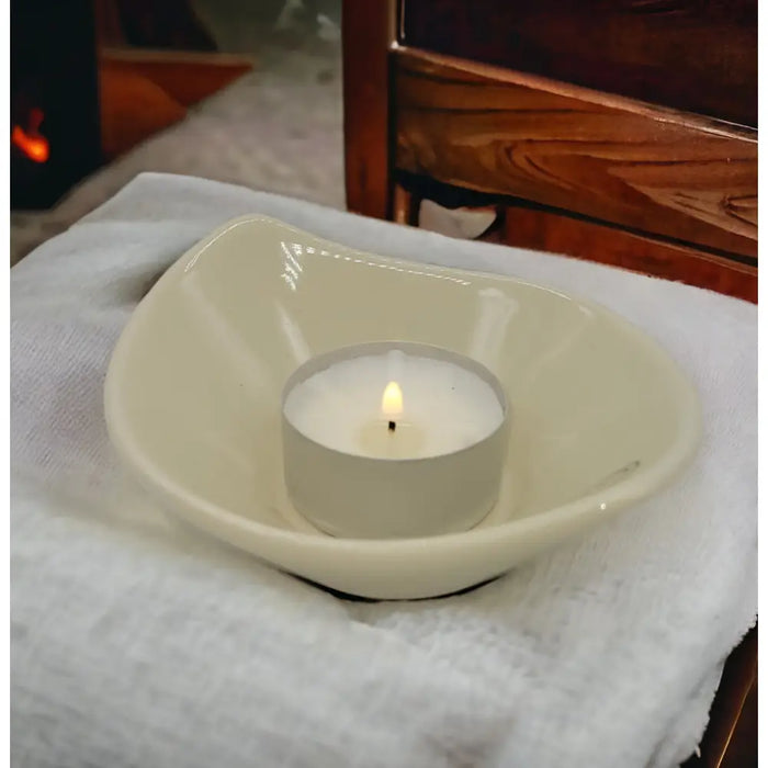 Cream-colored ceramic heart-shaped candle holder with a lit white tea light on a small leaf-shaped ceramic plate