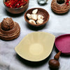 Cream-colored ceramic bowl with smooth curved rim and subtle glossy finish shown with small leaf-shaped plate in olive green brown and ivory