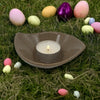 A small leaf-shaped ceramic plate in brown holds a matte ceramic candle holder with a lit tea light candle
