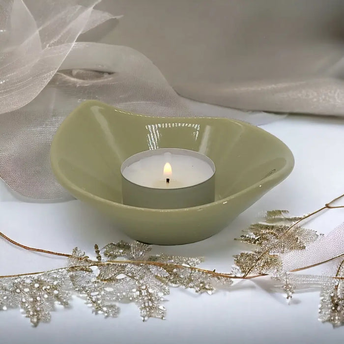 A small olive green ceramic leaf shaped plate holding a lit white tea light candle