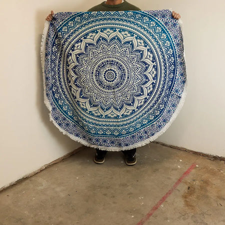 A small cotton beach towel with a blue and white mandala pattern and fringed edges measuring 130cm round