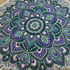A small cotton mandala roundie blanket with deep green, royal blue, and cream intricate patterns measuring 130cm