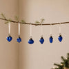 Set of six cobalt blue mouth-blown glass baubles with metallic caps hanging from a pine branch