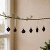 A set of dark glossy mouth-blown glass baubles shaped like heart star sphere acorn and teardrop hanging on white ribbons