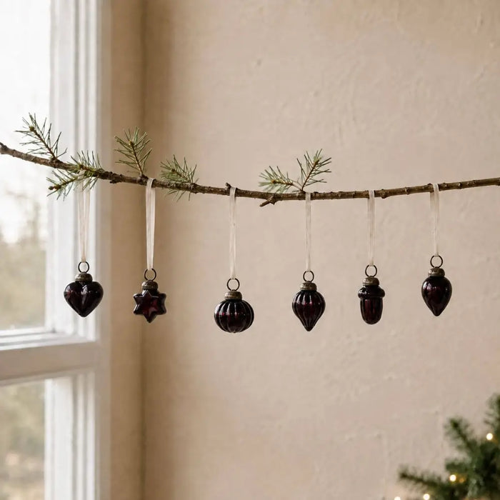 A set of dark glossy mouth-blown glass baubles shaped like heart star sphere acorn and teardrop hanging on white ribbons