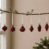 A set of six deep red mouth-blown glass baubles hanging on a pine branch with white ribbons and metallic caps
