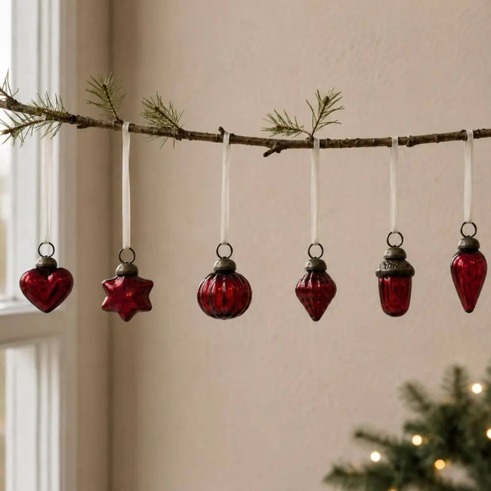 A set of six deep red mouth-blown glass baubles hanging on a pine branch with white ribbons and metallic caps