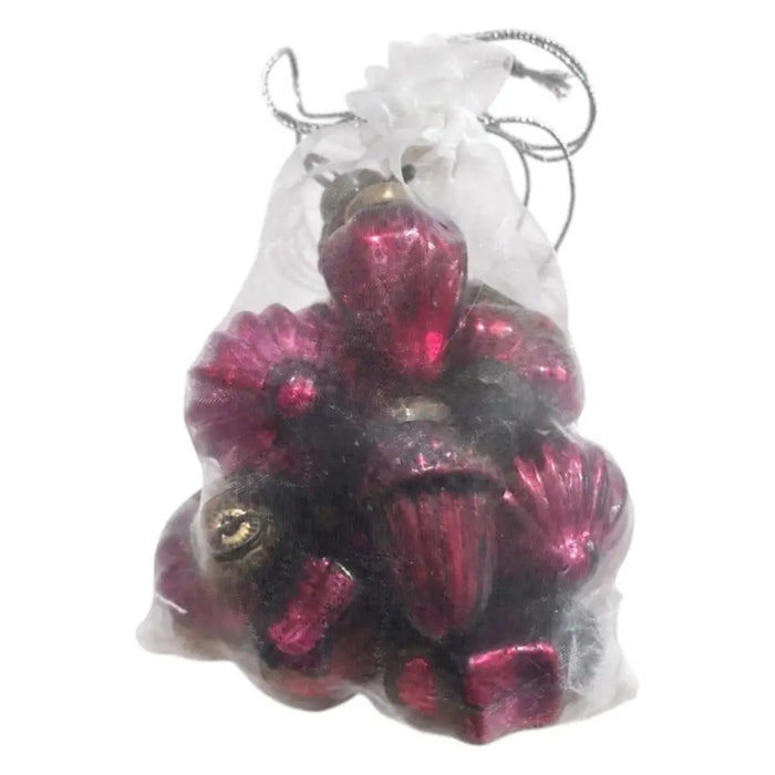 A collection of ruby mouth-blown glass baubles in acorn and flower shapes inside a sheer white drawstring bag