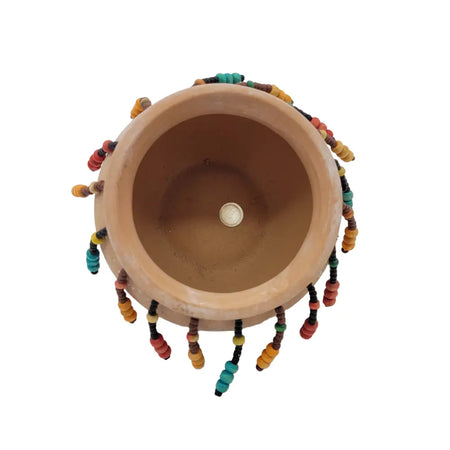 Small natural terracotta plant pot with colorful red orange yellow green and black beaded tassels on the rim