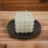 Small oval ceramic plate in white or blue holding a white cube candle with a bubbly textured surface and single wick
