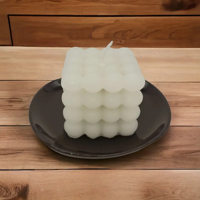 Small oval ceramic plate in white or blue holding a white cube candle with a bubbly textured surface and single wick