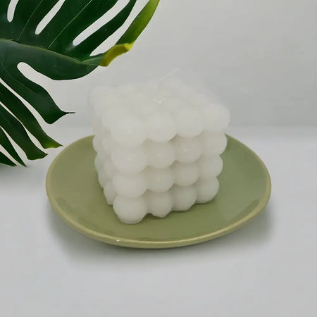 Small oval ceramic plate in sage green holding a white cube candle with a textured bubble surface