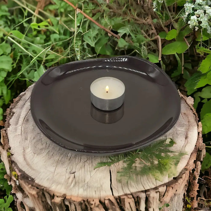 Small oval black ceramic plate holding a lit white tea light candle shown in a home setting