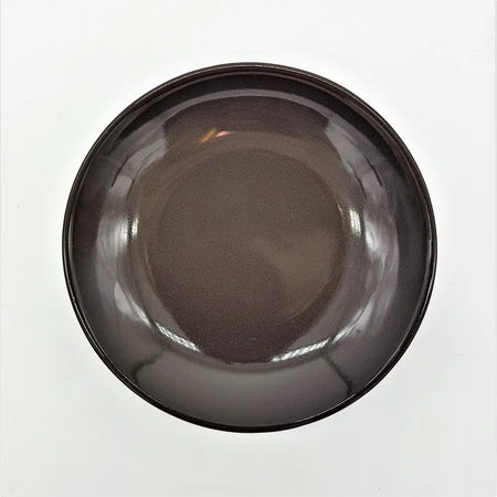 A small round ceramic plate in brown or ivory shown with a sleek dark gray glossy ceramic bowl with smooth rounded rim
